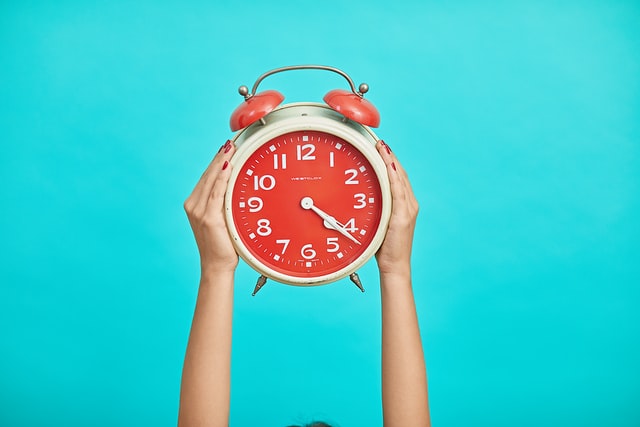 Tow hands holding up a red alarm clock showing the time is right to refinance
