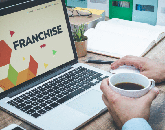 hands holding coffee cup in front of laptop displaying "Franchise"