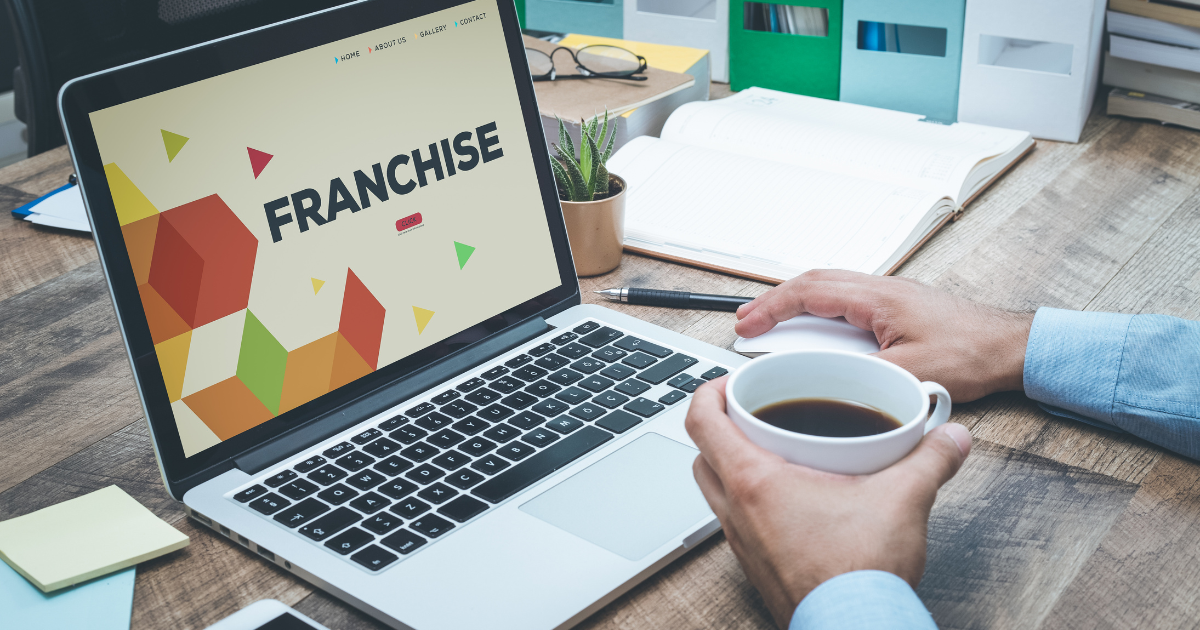 hands holding coffee cup in front of laptop displaying "Franchise"